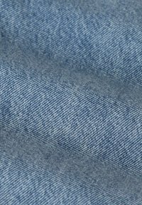 Tissu en denim bleu clair, présentant un tissage texturé avec un motif sergé diagonal. Doux et légèrement délavé avec des nuances variables de bleu.