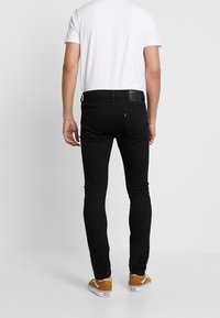 Jeans negros ajustados de denim con una textura suave. Presentan un parche de cuero en la cintura y costuras en contraste. Combinados con una camiseta blanca.