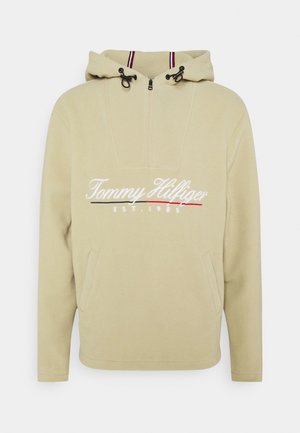 Sudadera beige de forro polar con capucha, cremallera frontal, cordón en la capucha, bolsillos delanteros y "Tommy Hilfiger EST. 1985" bordado en el pecho.