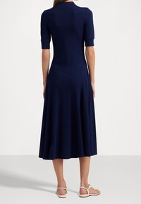 Námořnické modré šaty s přiléhavým korzetem a rozšířenou sukní. Mají krátké rukávy a límec ve stylu polo, vyrobené z hladkého džersejového materiálu.