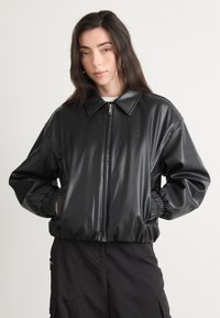 Giacca bomber nera in ecopelle con zip frontale, colletto ampio e polsini elasticizzati. Dettaglio logo discreto sul petto.