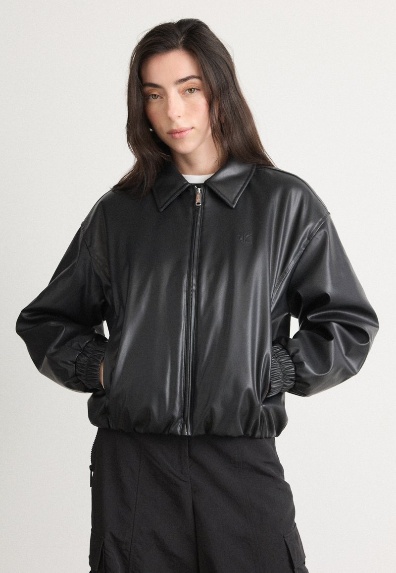 Giacca bomber nera in ecopelle con zip frontale, colletto ampio e polsini elasticizzati. Dettaglio logo discreto sul petto.