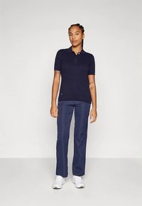 Μπλε ριμπ μπλούζα πόλο με κοντά μανίκια, συνδυασμένη με μπλε παντελόνι ραμμένο και λευκά αθλητικά παπούτσια, με κλασικό σχεδιασμό γιακά.