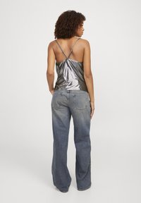 Top senza maniche di un argento metallico con spalline sottili, abbinato a jeans flare in denim blu a vita alta. Texture liscia, dettagli minimi.