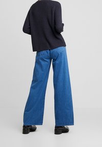Sweter w kolorze granatowym, dzianinowy, o luźnym kroju, w połączeniu z szerokimi jasnoniebieskimi dżinsami, noszony z czarnymi botkami na obcasie.