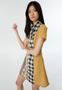 Vestido corto con un diseño de parcheado que incluye varias telas estampadas, como amarillo, cuadros, flores y estampados a rayas. Cuello y mangas cortas.