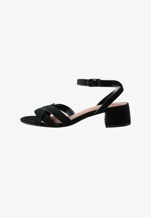 Sandalo aperto in suede nero con cinturini incrociati, fibbia alla caviglia e tacco basso a blocchetto.