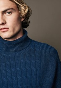 Blauer gestrickter Rollkragensweater mit geripptem Kragen und strukturiertem Zopfmuster, das eine weiche, leicht raue Wolloberfläche aufweist.