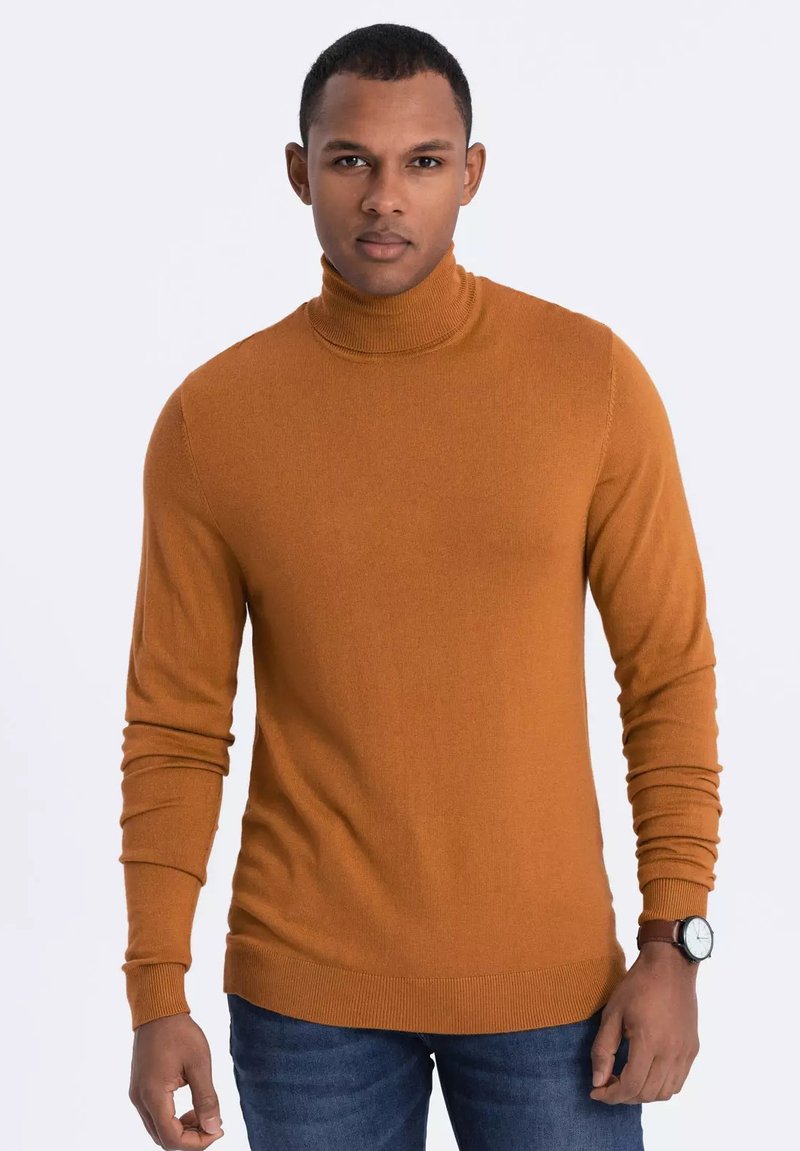 Ockerfarbener Rollkragenpullover aus einem weichen Strickstoff mit langen Ärmeln. Hat eine figurbetonte Silhouette und gerippte Bündchen und Saum. Kombiniert mit blauen Jeans.