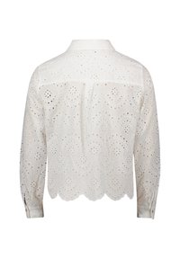 Weiße Bluse aus Spitzenstoff mit gewelltem Saum, langen Ärmeln und Kragen. Der Stoff zeigt ein Muster aus runden Augen und floralen Motiven.