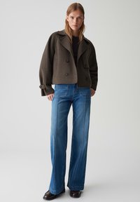 Gekürzte olivgrüne Wolljacke mit doppelreihigen Knöpfen, kombiniert mit hochgeschnittenen blauen Denim-Bootcut-Jeans mit genähten Nähten.