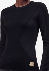 Pull noir ajusté à manches longues avec motif en maille géométrique texturée et petit logo beige "A|X" en bas à gauche devant.