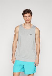 Graues Nike-Trägershirt mit rundem Ausschnitt; ausgestattet mit schwarzem Nike-Logo. Kombiniert mit hellblauen Shorts, die einen schwarzen Logo-Akzent aufweisen.
