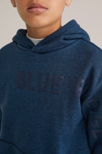 Temno modra kapuca iz teksturirane tkanine, z velikim tiskom "BLUE" na sprednji strani in besedilom "RIDGE" ob rokavu.