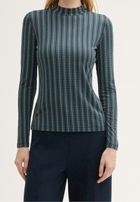 Maglietta a maniche lunghe con collo alto di colore verde scuro, caratterizzata da un motivo a righe verticali di rettangoli blu chiaro e bianchi, design aderente e texture liscia.