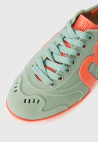 Light green sneaker with textured finish, coral accents, and rounded toe. Features lace-up design and perforated details on the side.