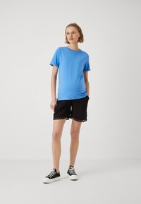 T-shirt bleu à manches courtes en matériau doux, associé à un short noir avec des bords festonnés, et des baskets noires avec des semelles blanches.