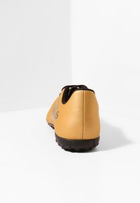 Keltainen urheilukenkä, jossa on tekstuuripinta, musta pohja ja hillitty brändäys kantapäässä. Pyöreä kärki ja matala malli ketteryyttä varten.
