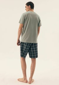 Jasnozielona koszula z krótkim rękawem w połączeniu z granatowymi szortami w kratę, z niebieskimi i białymi akcentami, sięgająca do kolan, gładka tekstura.