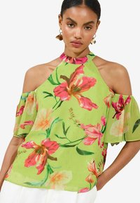 Blusa floreale in chiffon verde brillante con design a spalle scoperte, caratterizzata da fiori rosa e arancioni e un colletto a balze.