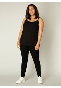 Zwarte mouwloze top gecombineerd met zwarte leggings, gemaakt van zachte stof. Draag het met witte sneakers voor een casual outfit.