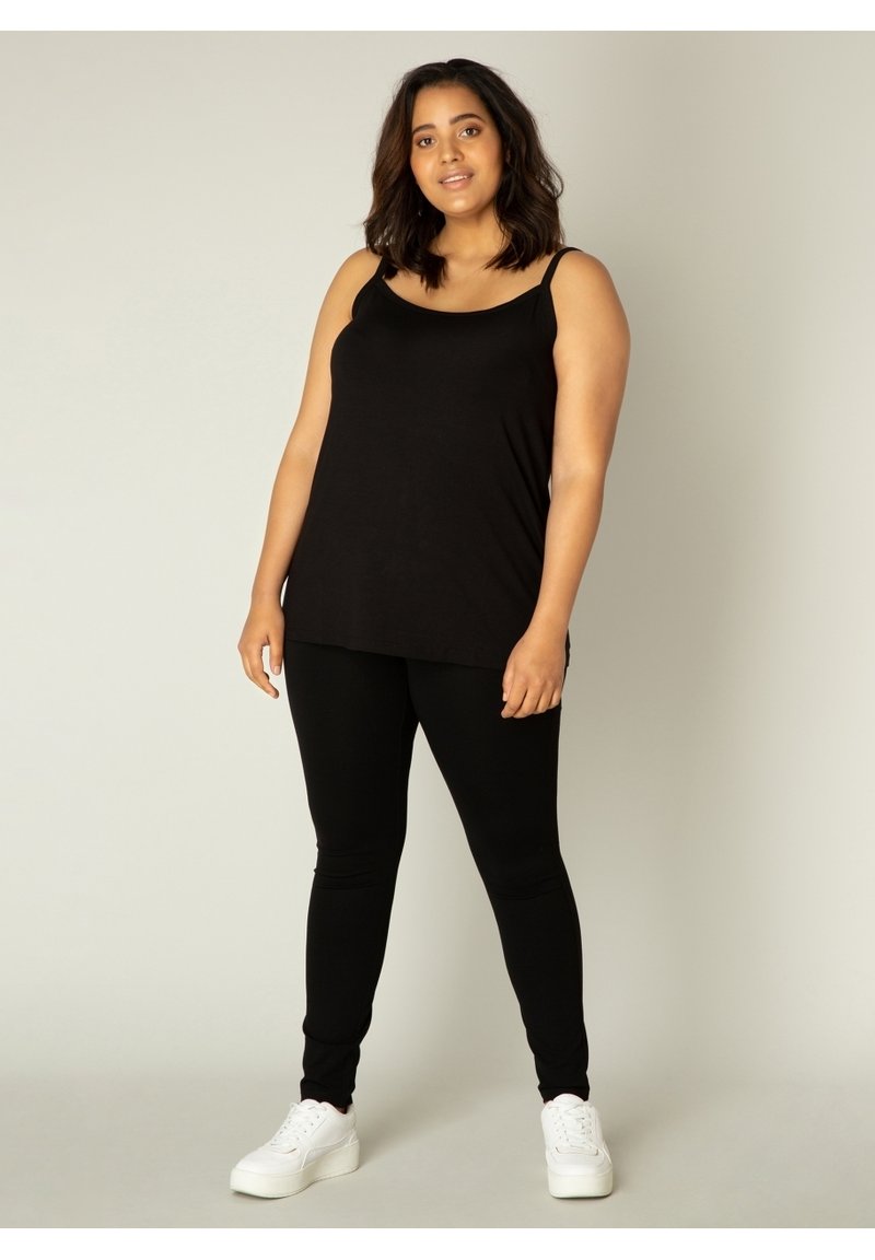 Zwarte mouwloze top gecombineerd met zwarte leggings, gemaakt van zachte stof. Draag het met witte sneakers voor een casual outfit.