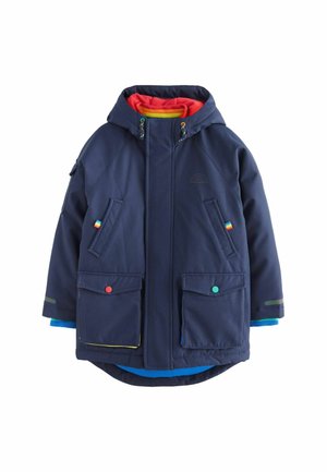 Marineblauwe waterdichte jas met capuchon, met een rode binnenvoering, twee ruime voorvakjes en kleurrijke accentknopen.