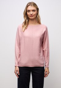Helle rosa Langarm-Bluse mit Rundhalsausschnitt und weicher Textur. Sie hat ein schlichtes Design und wird mit dunklen Jeans getragen.