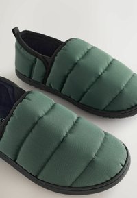 Zelené prešívané papuče na slip-on s čiernou podrážkou a lemovaním. Hladká, mäkko vystlaná látka s horizontálnym prešívaním, navrhnutá na pohodlie.