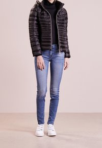 Svart puffjacka med horisontell quiltad design, dragkedjeslutning och huva. Kombinerad med ljusblå skinny jeans och vita sneakers.