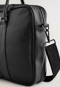 Black leather bag with a textured surface, zip closure, and a removable strap featuring a metal clip and reinforced stitching.