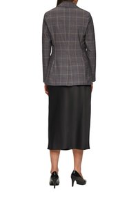 Op maat gemaakte grijze blazer met een ruitpatroon, gecombineerd met een zwarte satijnen midi-jurk en zwarte hoge hakken. Achteraanzicht van de outfit.