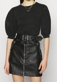 Černý top s balónovými rukávy vyrobený z bavlny, spárovaný s černou koženou miniskirt s vysokým pasem, která má přední zip a boční kapsy.