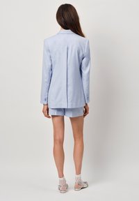 Lichtblauwe blazer met een enkele achterkantventilatie, gecombineerd met bijpassende shorts. Heeft een op maat gemaakte uitstraling en knoopmanchetten. Draagt een paar kanten sokken en schoenen.