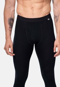 Leggings neri realizzati in un tessuto elasticizzato, con un design aderente, vita elasticizzata e un'apertura frontale per l'accessibilità.
