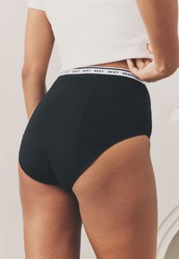 Culotte noire taille haute avec ceinture élastique blanche à logo, tissu lisse et design sans coutures, avec des détails de couture minimaux.