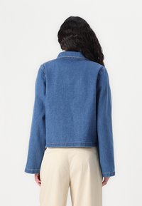 Veste en jean courte de couleur bleu moyen avec manches longues, col et ourlet droit. Texture lisse et détails de coutures minimaux.