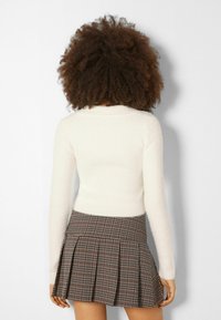 Vit ribbad stickad tröja med långa ärmar, tillsammans med en brun rutmönstrad plisserad kjol med vertikala linjer och utställd fåll.