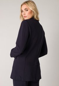 Donkerblauwe op maat gemaakte blazer met lange mouwen, gestroomlijnde silhouette en ventilerende rug. Gladde stof met schone naden en modern ontwerp.