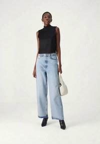 Musta hihaton toppi, korkea kaula-aukko, yhdistetty vaaleansinisiin leveälahkeisiin farkkuihin. Malli pitää pientä valkoista käsilaukkua ja käyttää mustia korkokenkiä.