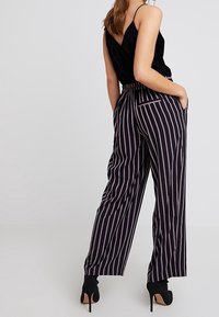 Pantalones de rayas verticales en negro con una cintura alta, que presentan un corte relajado y bolsillos. La tela tiene una textura suave.