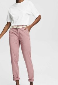 T-shirt blanc à manches courtes associé à un pantalon rose clair à ourlet retourné, comportant une ceinture tressée crème et un design à jambes droites.