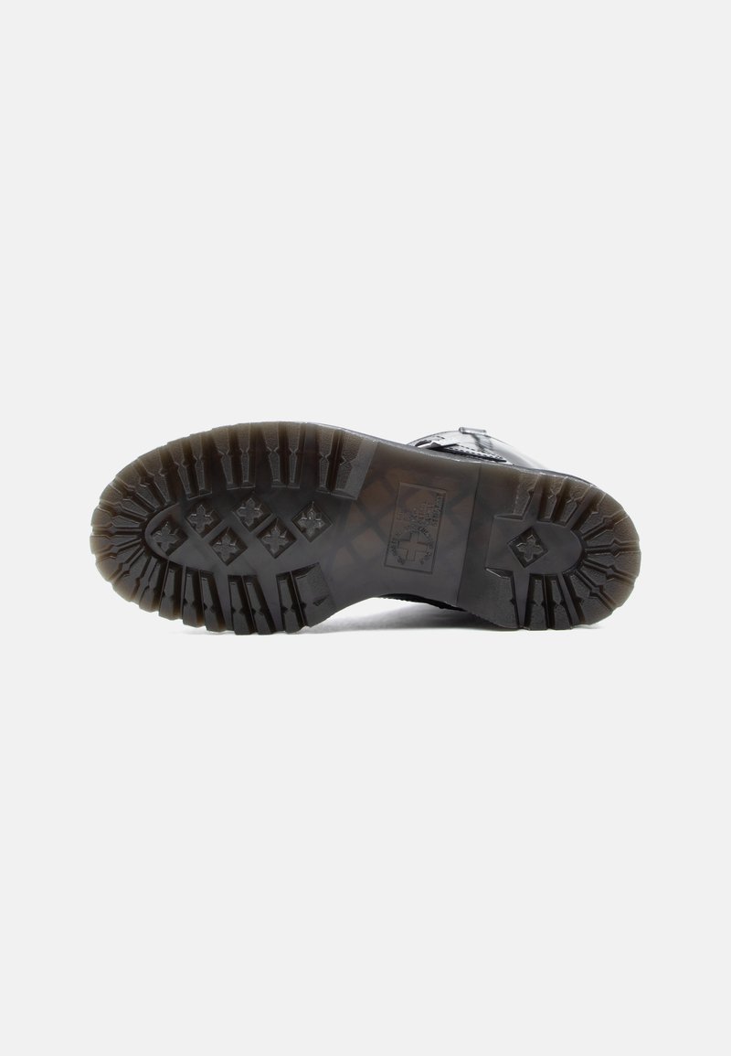 Schwarze Stiefelsohle mit tiefen Profilen und kreuzförmigen Mustern vor einem schlichten weißen Hintergrund.