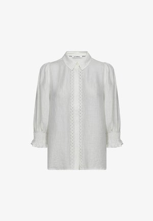 Balta teksturēta blūze ar spārniem piedurknēs, mazu apkakli, pogu rāvējslāni ar apļveida mežģīņu apdari un cieši savērptiem volānu aprocēm.