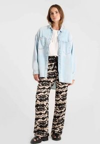 Chemise en denim bleu clair portée sur un t-shirt blanc, associée à un pantalon noir à motifs marron clair et des sandales noires.