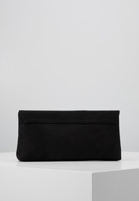 Pochette rectangulaire noire avec un rabat, exposée sur un piédestal blanc contre un fond gris clair.