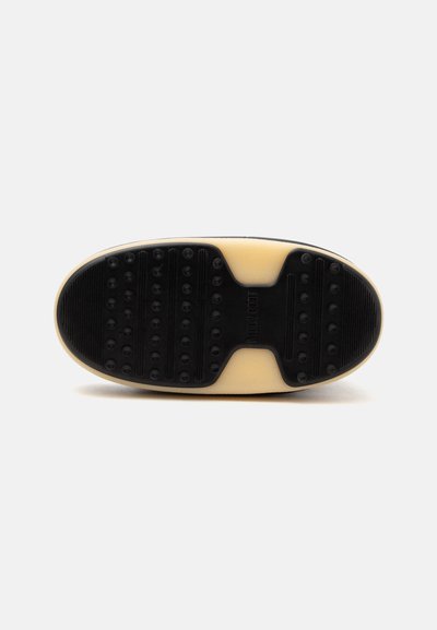 Semelle de chaussure avec des sections de grip en caoutchouc noir comportant des protubérances rondes sur une base beige, vue par le dessous.