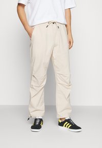 Beige letvægts cargo-bukser med elastisk talje, sidelommer og justerbare manchetter. Sammen med sorte sneakers med gule striber.