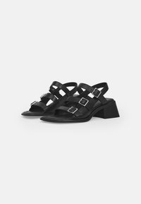 Black leather sandals featuring three adjustable straps with silver buckles, a square toe, and a textured block heel.