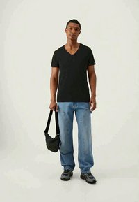 Black cotton v-neck t-shirt paired with light blue loose-fitting jeans, black crossbody bag, and gray sneakers. Simple and casual design.